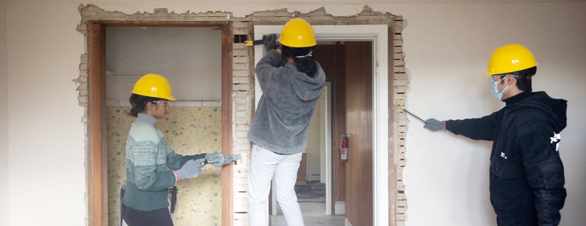 3 people in yellow hard hats deconstructing a room