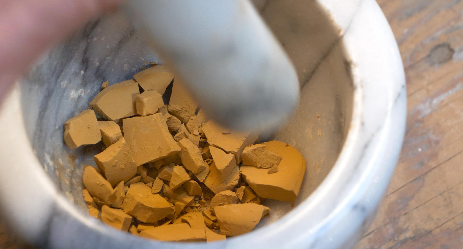 A person stirring auburn powder in a bowl, creating a pigment
