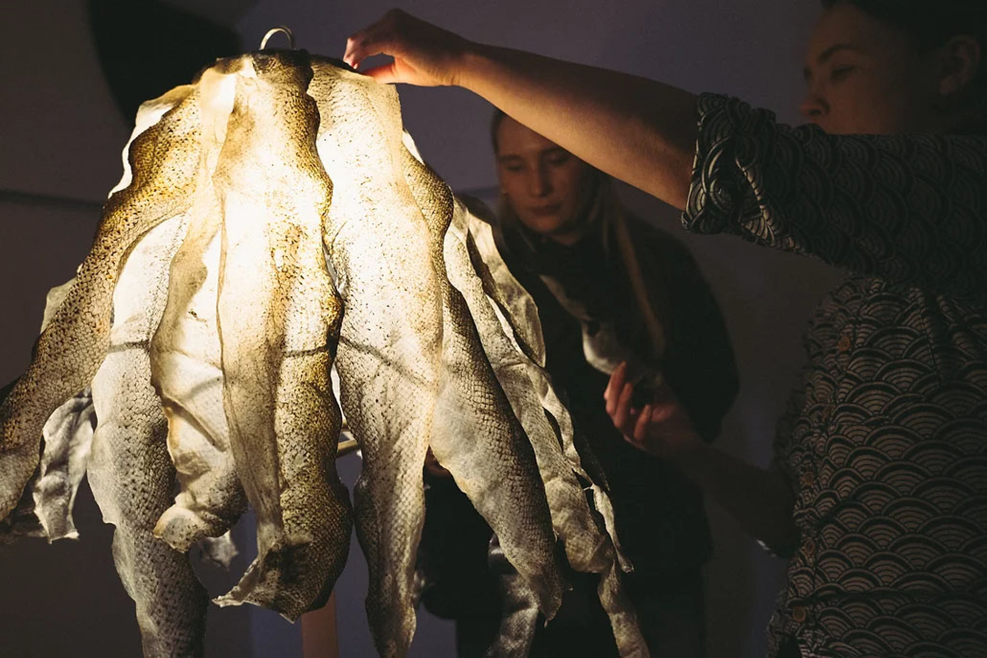 A woman holding a large fish skin light pendant hanging from a ceiling