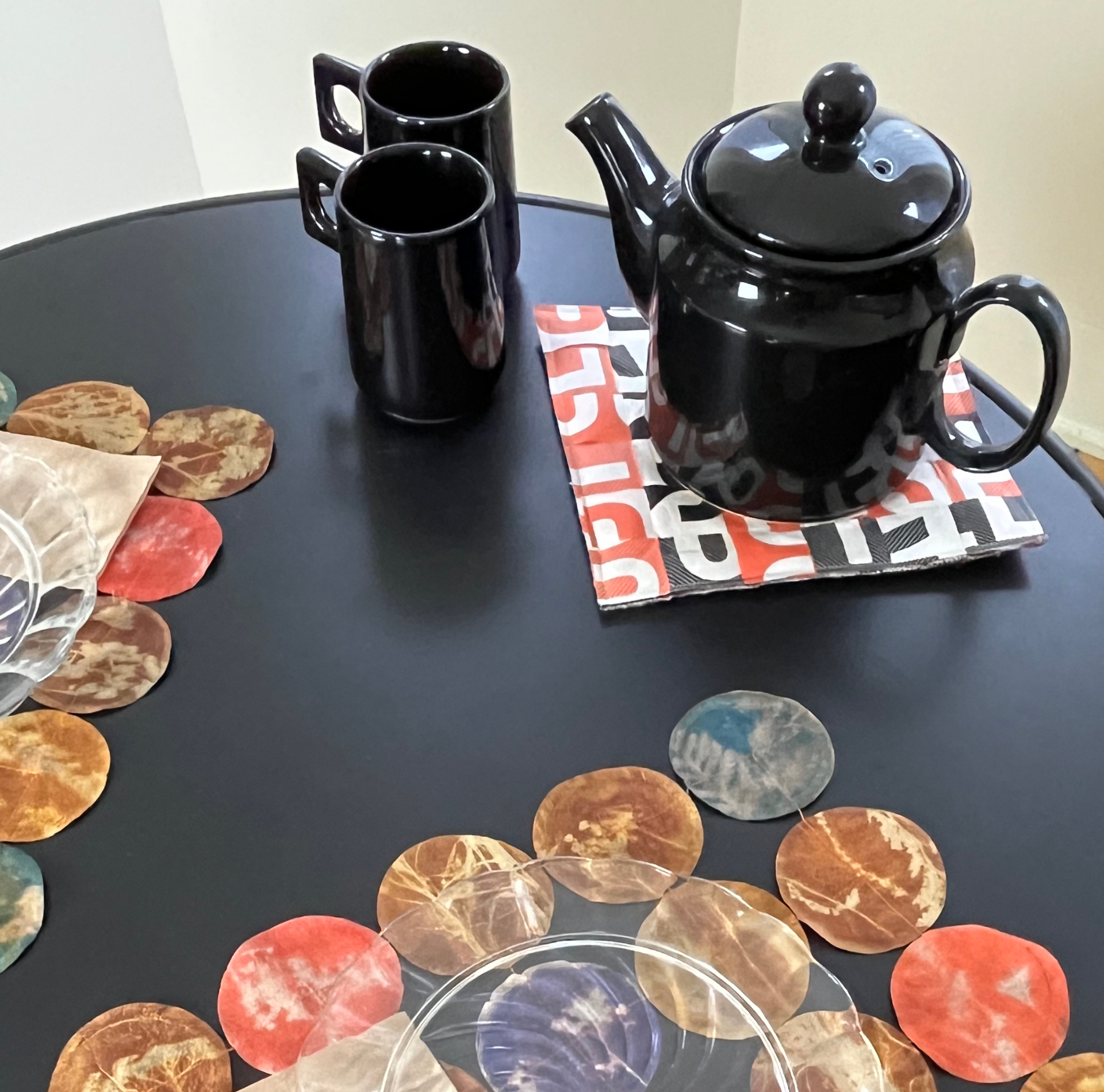 A black table with placemats made from used tea bags and a trivet made from coffee packaging and an old wool blanket.