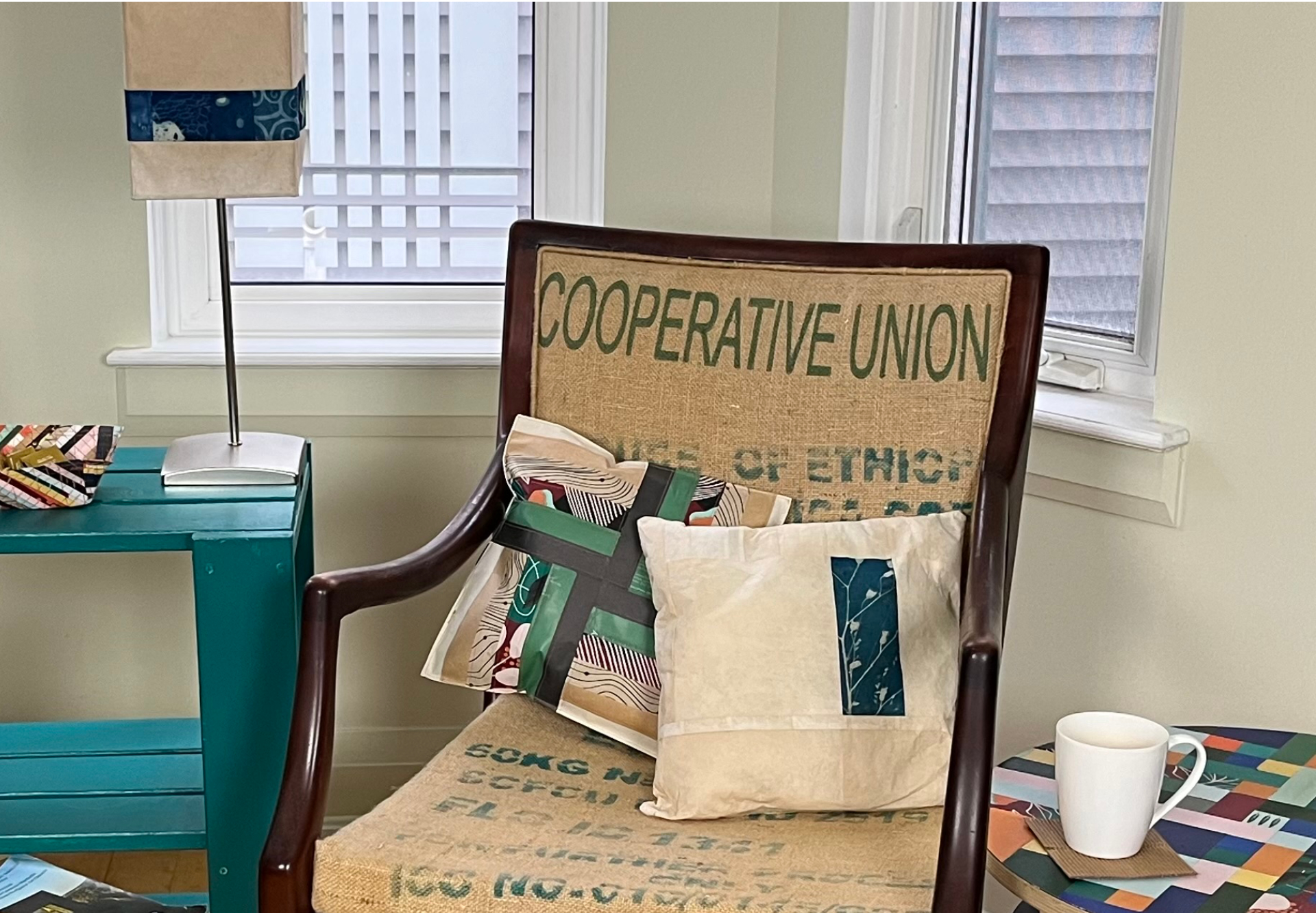 A living room space, with a chair upholstered in burlap coffee sack fabric, and decorated with accessories made from used coffee filters and coffee packaging.