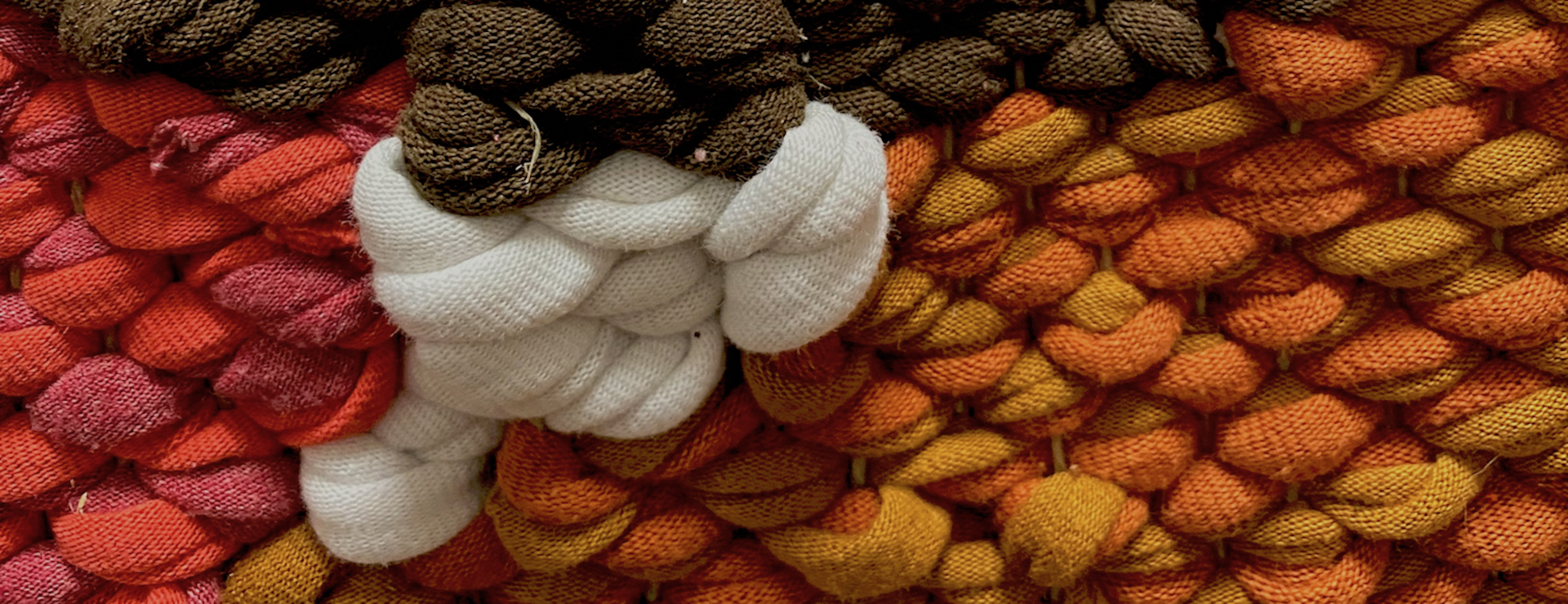 Close up of a weaving in browns and oranges. It is made of t-shirt fabric and you can see the hemp cord warp threads.