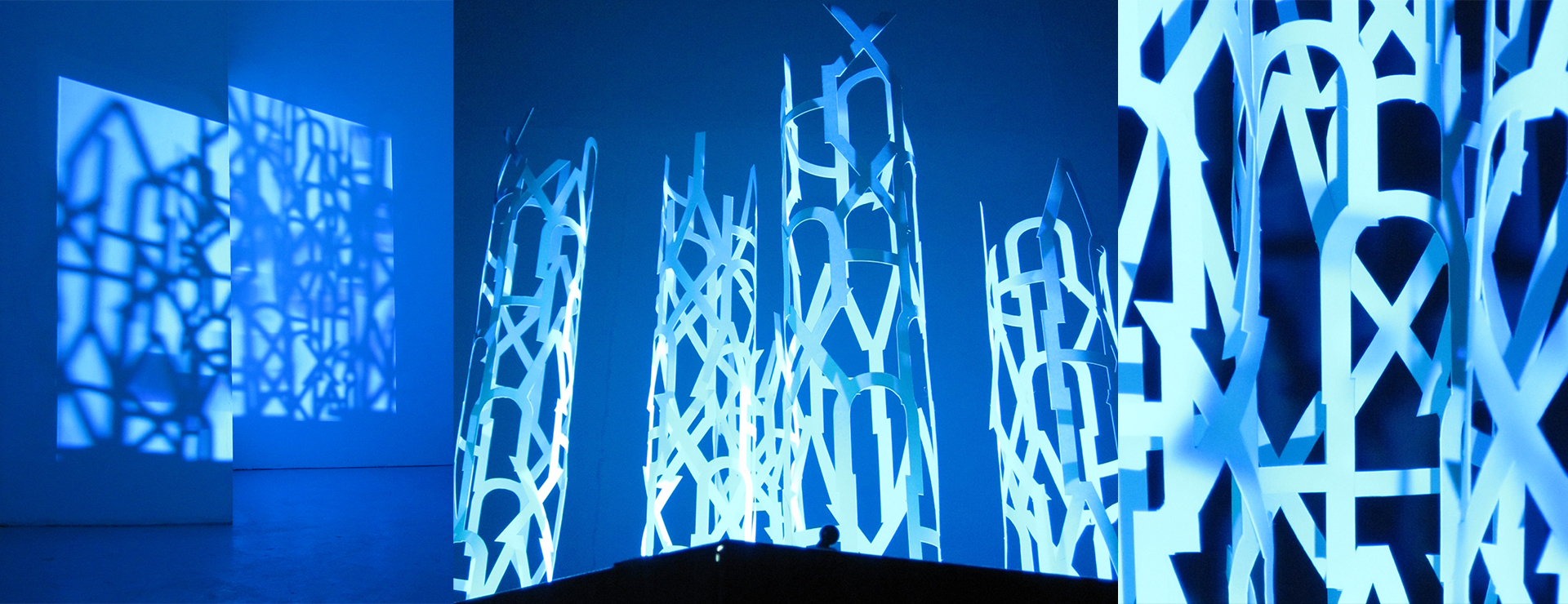 Sculpture composed of letterforms with shadow cast onto gallery wall with blue light