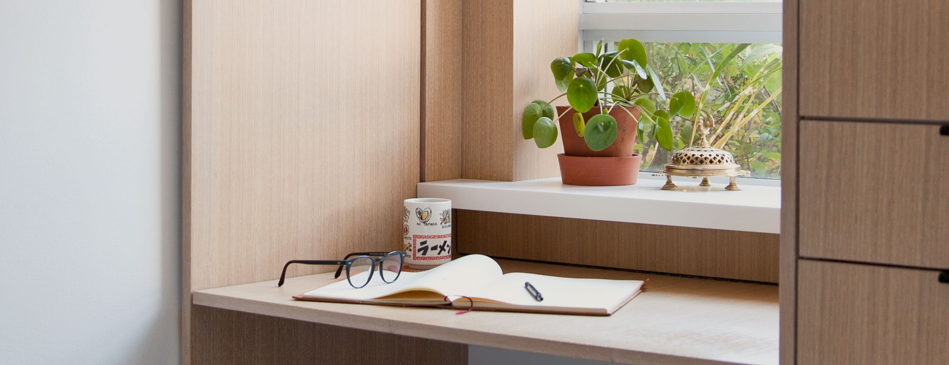 Eyeglasses and a notebook on a desk in front of a window with plants in view