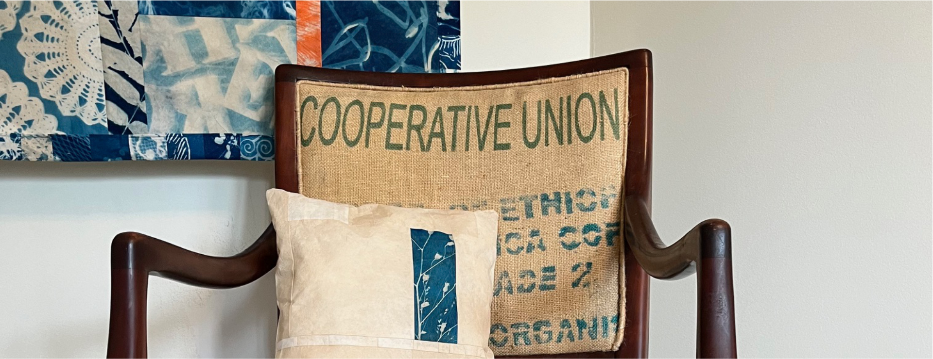 An armchair upholstered in burlap from a coffee sack, with a pillow and wall hanging made from coffee filter paper with cyanotype imagery.